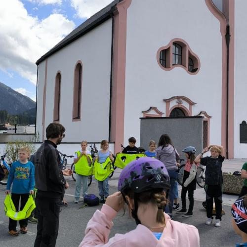 Die Kinder der 4. Klasse stehen im Kreis vor der Dekanatskirche in Breitenwang - die Lehrerin geht reihum und sammelt die Warnwesten ein