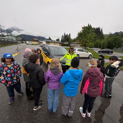 Eine Gruppe Kinder steht vor dem ÖAMTC Auto "Hallo Auto" und hört den Erklärungen des ÖAMTC Mitarbeiters zu