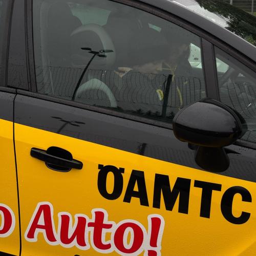 Man sieht die rechte Vordertüre des schwarzen ÖAMTC Autos zur Aktion Hallo Auto, auf der Türe klebtein Bild mit dem Schriftzug ÖAMTC und Auto