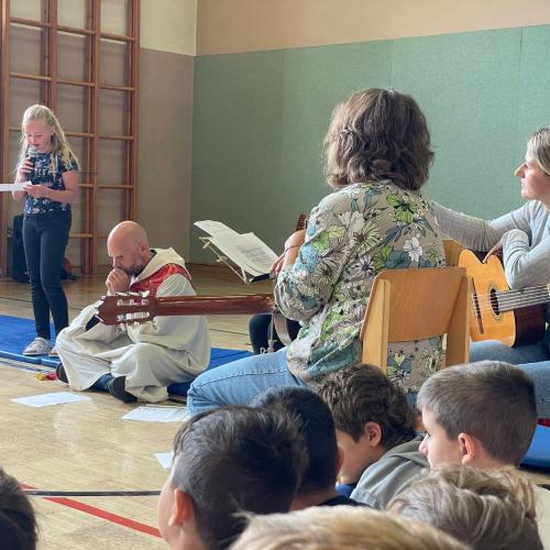 Eine Schülerin liest die Lesung, im Vordergrund sitzen zwei Lehrerinnen mit den Gitarren