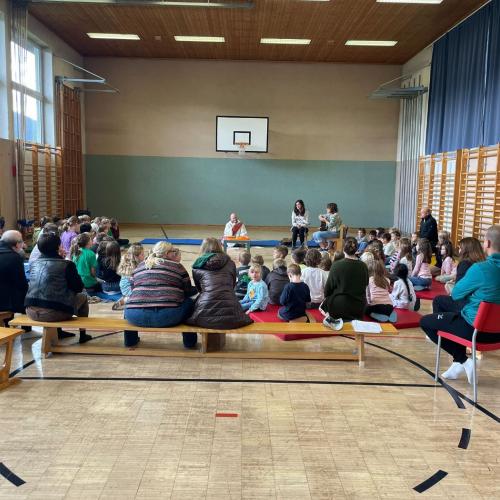 Turnsaal - Schulanfangsandacht - man sieht die Eltern von hinten  - sie sitzen auf Langbänken