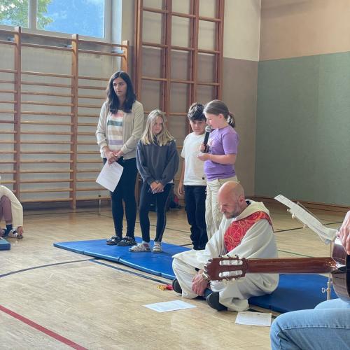 Die Religionslehrerin steht gemeinsam mit 3 Kindern neben dem Diakon und die Kinder sprechen Fürbitten