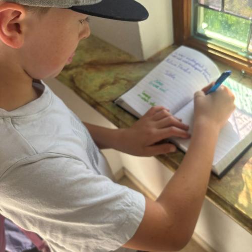 Ein Bub mit einer Schildkappe trägt sich ins Buch der Kapelle ein