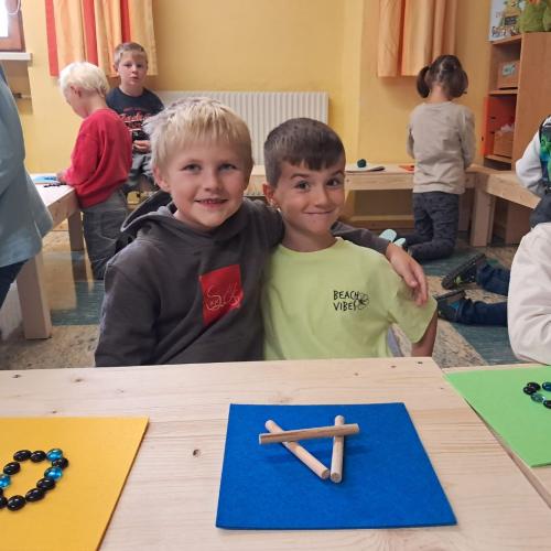 Man sieht einige Kinder in der Klasse, zwei Jungs sitzen vor ihren fertigen Buchstabenbildern