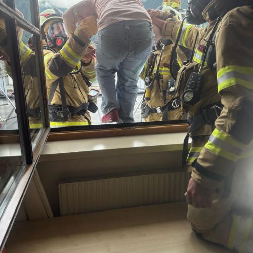 Ein Kind steigt mit Hilfe zeier Feuerwehrmänner auf das Flachdach des hinteren Einganges von wo es mit dem Bergekorb hinuntergebracht wird