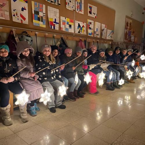 Die Kinder der 1 Klasse sitzen in der Schule auf der Bank in der Garderobe mit ihren gebalstelten "SternLaternen".