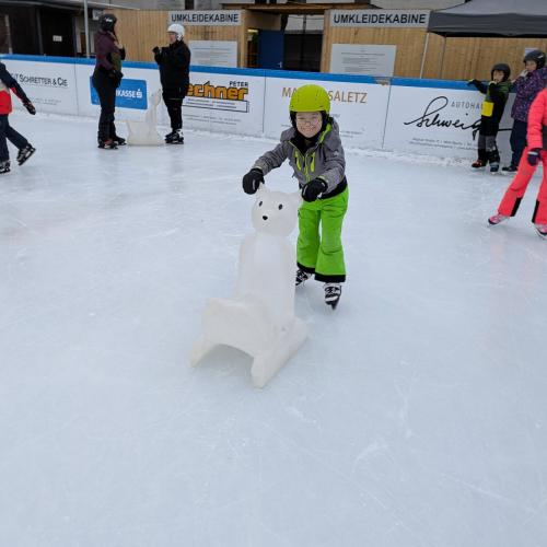 ein Kind fährt mit Hilfe eines "Eishbären" über den Platz