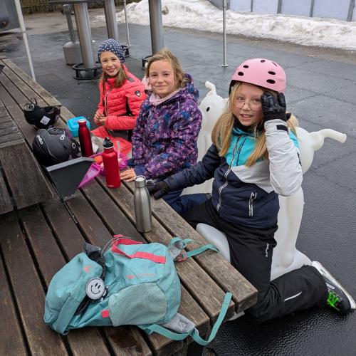 3 Kinder sitzen auf den "EIsbären" und benützen die Holzbank als Tisch für ihre Jause