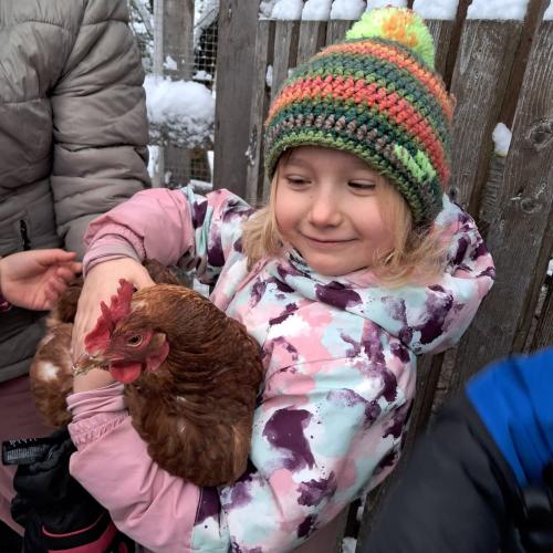 Ein Mädchen mit gestreifter Mütze hält mit strahlendem Gesicht ein Huhn im Arm