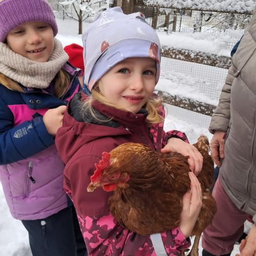 2 Mädchen stehen bei einem Zaun und eine hält ein braunes Huhn im Arm