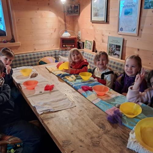 Die Kinder sitzen an einem langen Tisch mit bunten Tellern vor sich und filzen ein Schaf