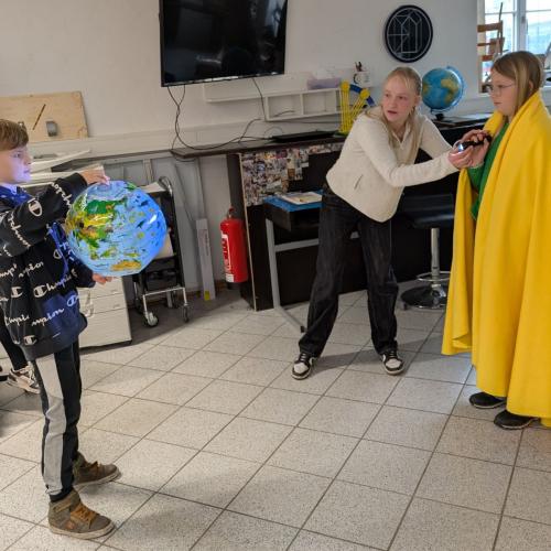 Ein Kind mit gelbem Umhang (die Sonne) leuchtet mit einer Taschenlampe auf einen Globus, um Tag und Nacht auf der Derde darzustellen