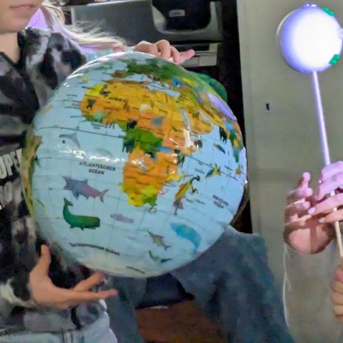 ein Kind hält einen Globus, ein anderes hält eine Kugel, die den Mond darstellt dazu