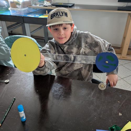 ein Bub hält das fertige gebastelete Model von Sonne, Erde und Mond in der Hand und zeigt es