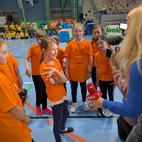 Einige Kinder der 3a, in orangen T-Shirts stehen bei einer Reporterin des ORF Tirol und geben ein Interview