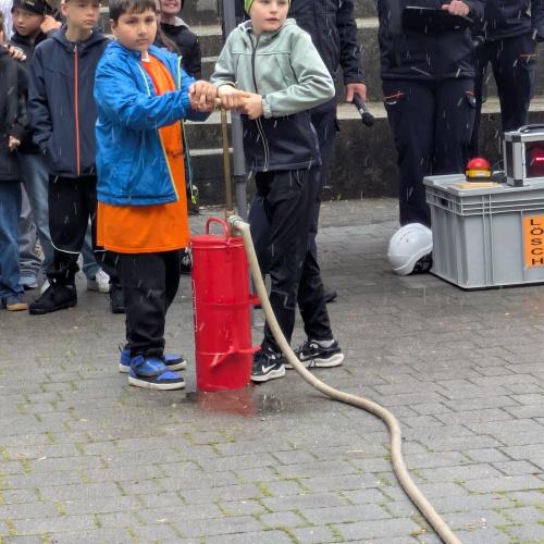 2 Kinder der 3a pumpen mit einer kleinen roten Handpumpe der Feuerwehr