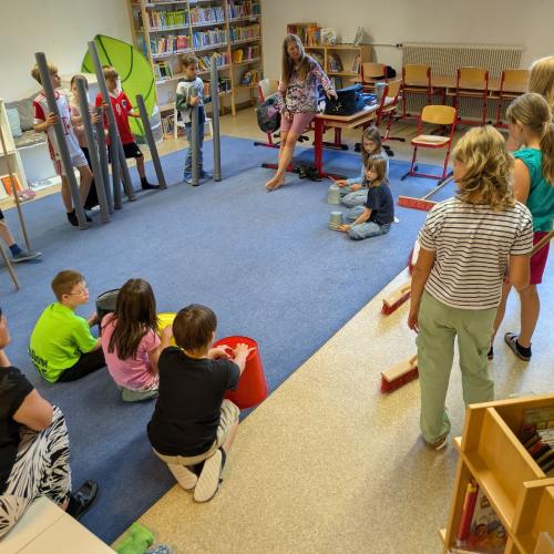 Alle Kinder stehen oder sitzen im Kreis mit außergewöhnlichen Musikinstrumenten wie Besen, bunten Blechkübeln, Holzstangen, Instalationsrohre usw.