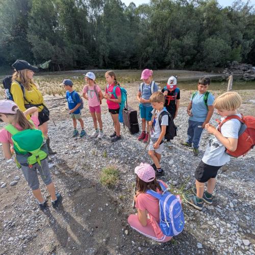 Die Kinder der Klasse stehen mit Sabine von Natopia im Kreis auf einer Schotterfläche am Lech