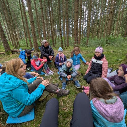 Alle Kinder sitzen am Waldboden und hören gebannt der NAturpädagogin zu, die eine Geschichte erzählt
