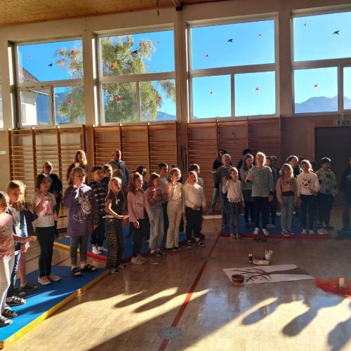 Die Kinder stehen im Halbkreis im Turnsaal und singen gemeinsam ein Lied
