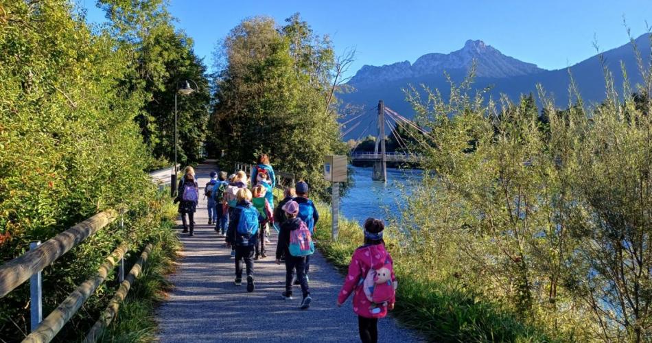 Blick auf Kindergruppe, die an  strahlendem Herbsttag am Lech entlang wandert.