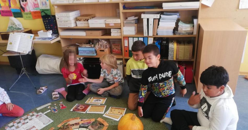 5 Kinder sitzen am Boden in der Klasse - vor ihnen ein Legekreis, ein Hokkaidokürbis und anderes Material zum Thema Kürbis