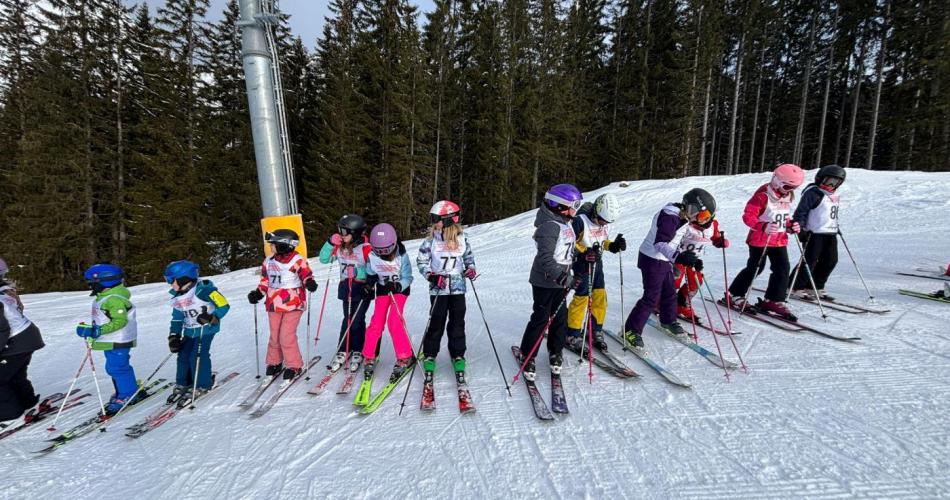 Kinder stehen in einer Reihen untereinander auf der Schipiste in Berwang, im Hintergrund Wald