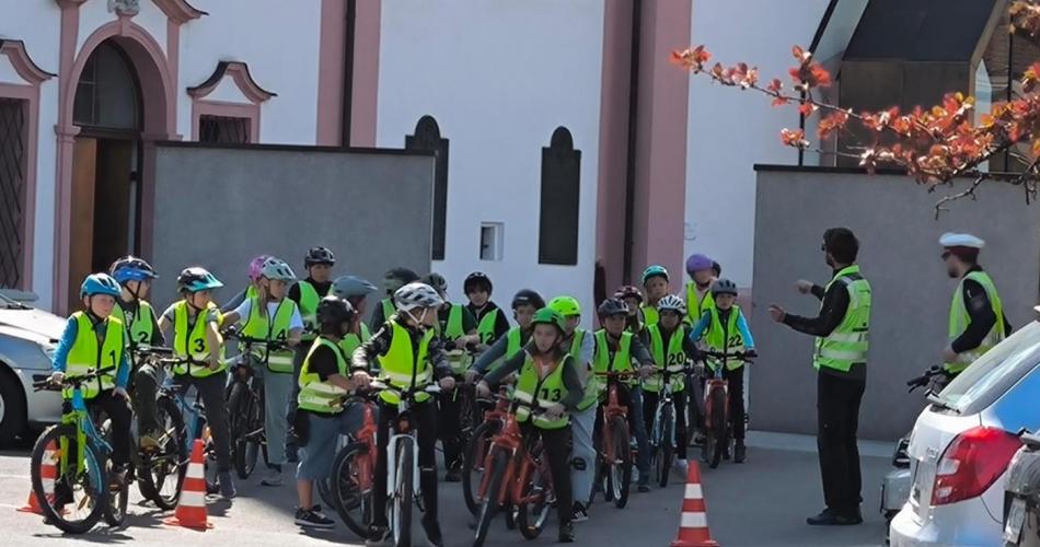 Vor der Dekanatskirche in Breitenwang stehen alle Kinder der 4. Klasse mit Fahrrädern, sie tragen gelbe Warnwesten, vor ihnen stehen 2 Polizisten