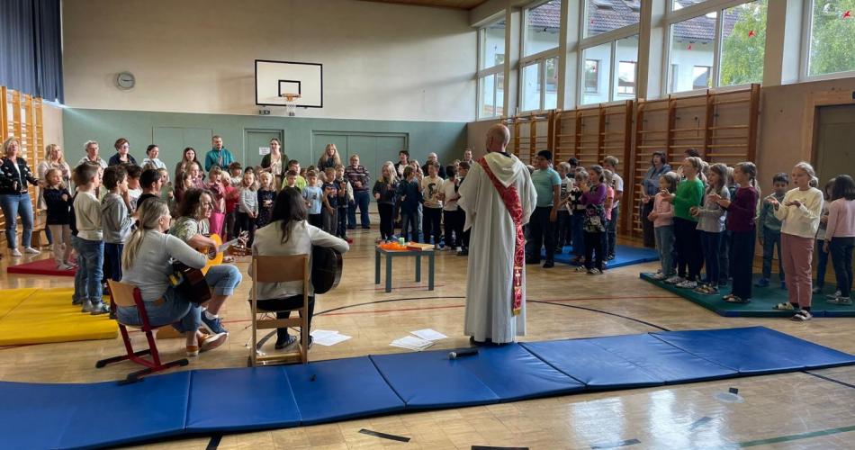 Im Turnsaal fand unsere gemeinsame Schulanfangsandacht mit Diakon Patrick Gleffe statt, Alle Kinder Lehrerinnen und einige Eltern sind versammelt.