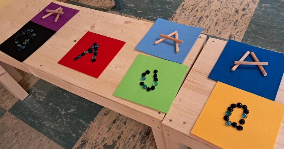 Auf buntem Papier sind mit verschiedenen MAterialien Buchstaben gelegt