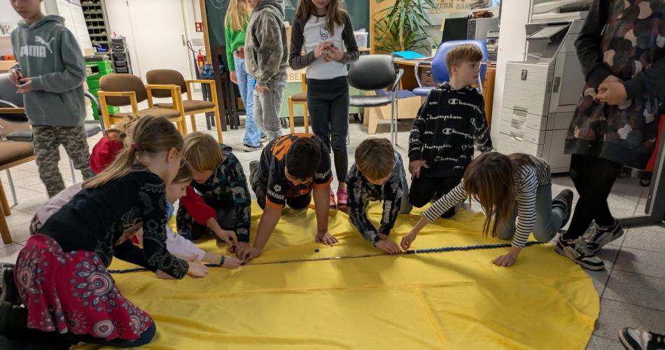 in einem Raum im Werkhaus Reutte sitzen die Kinder am Boden auf einem großen runden Tuch, das die Sonne darstellten soll